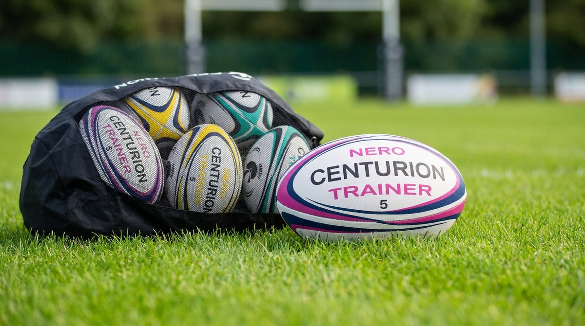 A black rugby bag filled with rugby balls sits on a green grass field, with one white rugby ball labeled 'NERO CENTURION TRAINER' in the foreground.